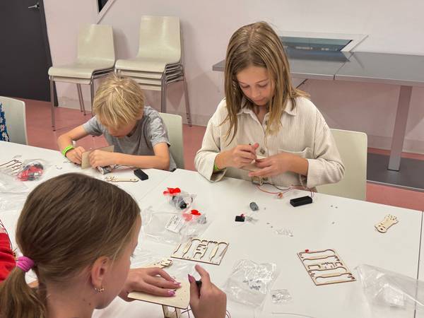 Three campers assembling wooden robot kits with motors and wiring