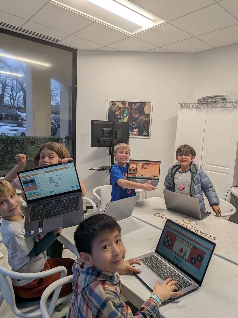 Five children holding up laptops showing their block-coding programs