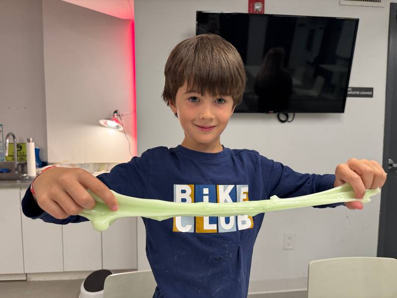 A boy stretching a long piece of green slime between his hands