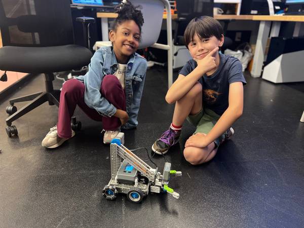 Two smiling kids next to a partially built robot