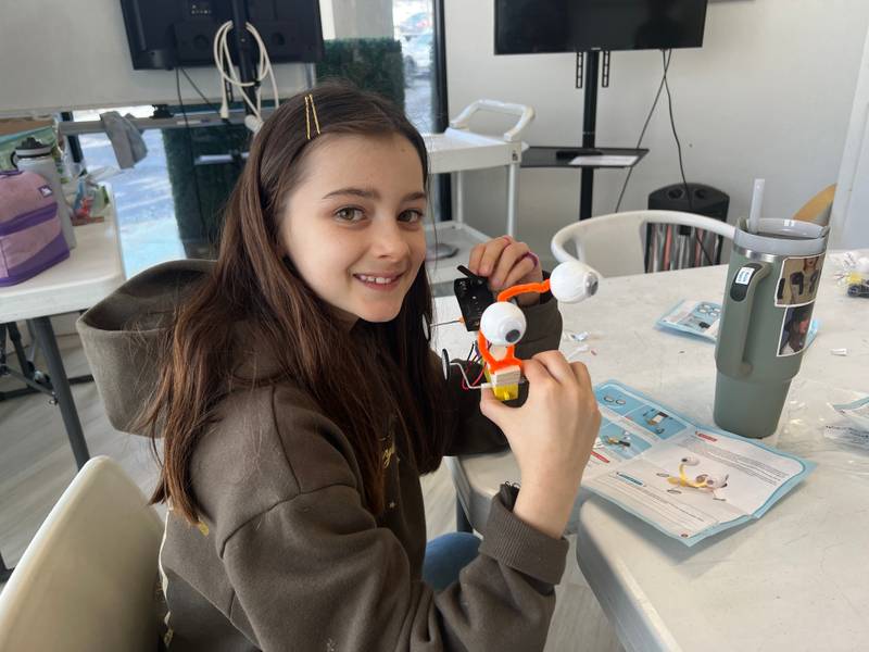 A girl holding up a moving robot with googly eyes she built at Genius Gems Millburn