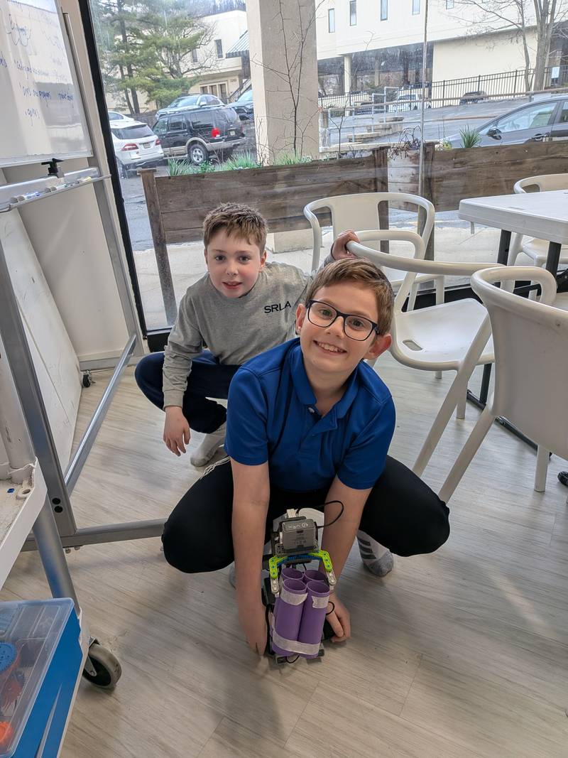 Two boys crouching beside the robot they built at Genius Gems Millburn
