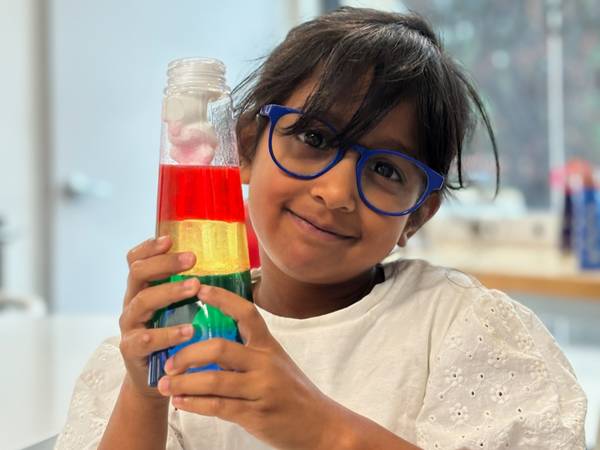 A camper holds up a rainbow density bottle from a chemistry lab