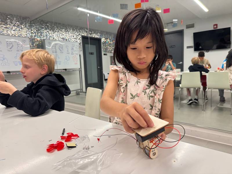 A girl working on a small wooden robot with wires at Genius Gems NYC