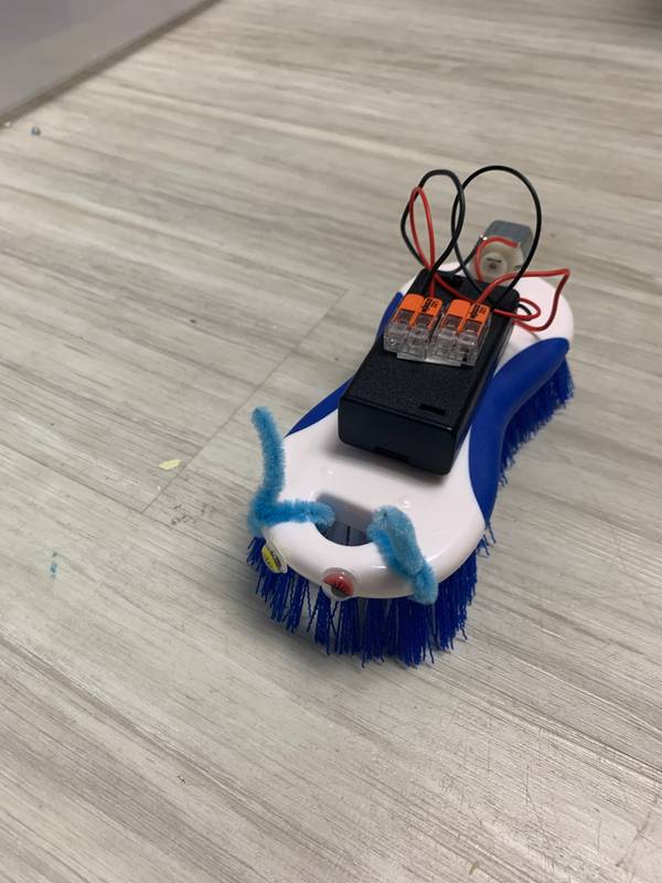 A finished brushbot — a scrub brush with a motor, battery pack and googly eyes, ready to scoot