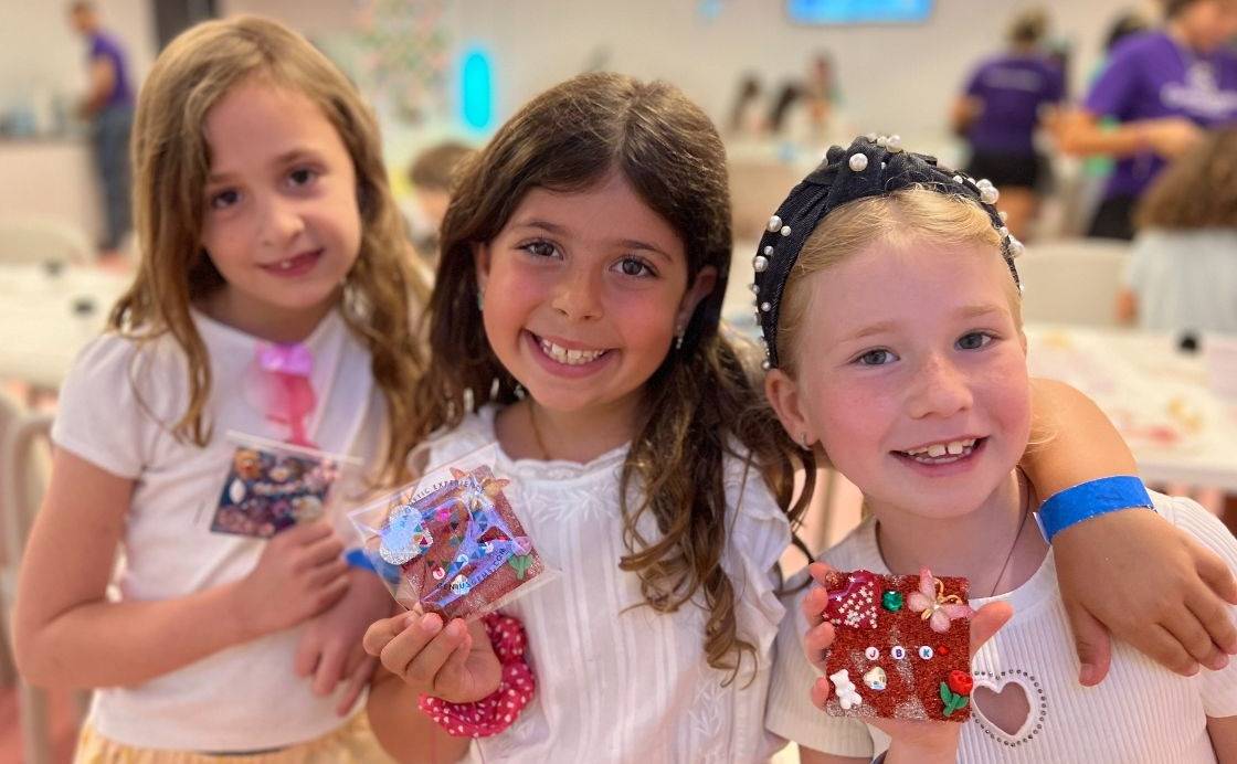 Three party guests in wristbands holding up the glitter tiles they designed at Genius Gems NYC