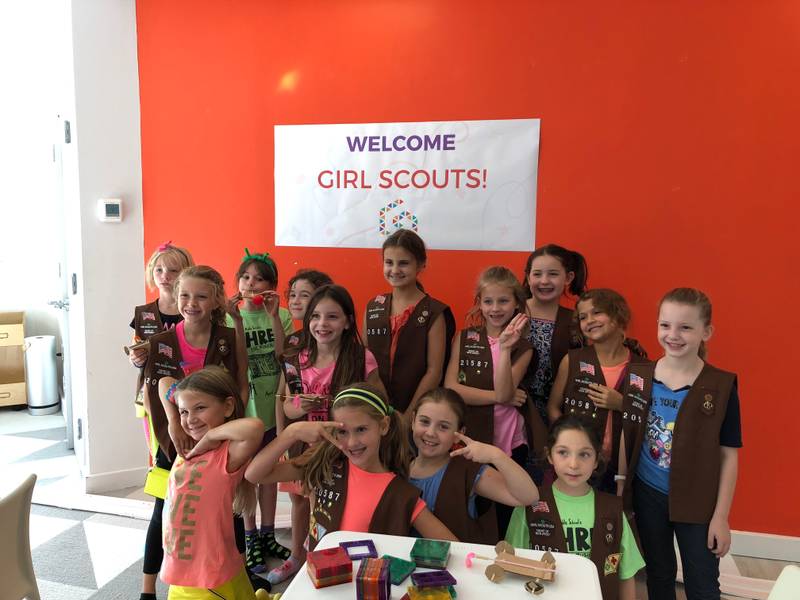A Brownie troop under a Welcome Girl Scouts banner at Genius Gems Millburn
