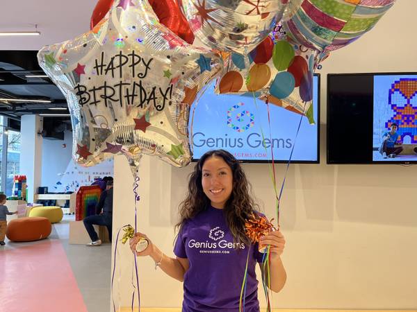 A Genius Gems party leader holding Happy Birthday balloons