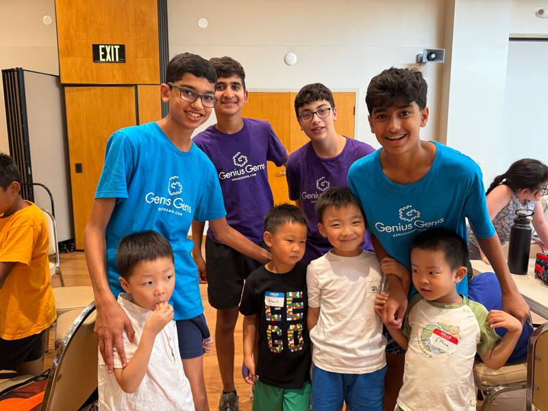 Four teen counselors-in-training in blue and purple Genius Gems shirts pose with four young campers in the Millburn summer camp hall.