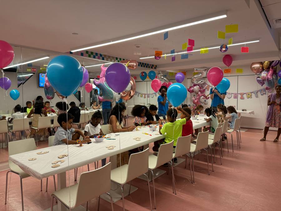 The Genius Gems NYC party room — a dozen kids at a long white table working on their project