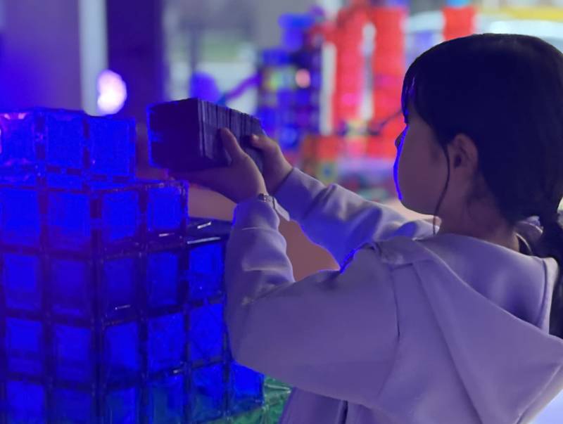 A girl stacking glowing blue magnetic tiles