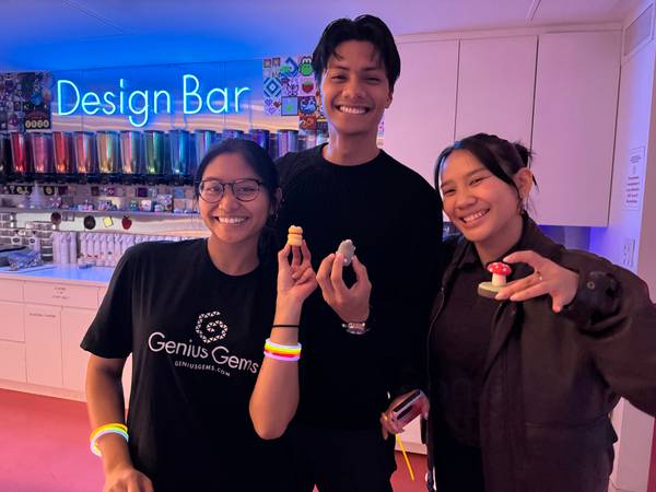 Three adults holding handmade bead charms under the blue neon Design Bar sign