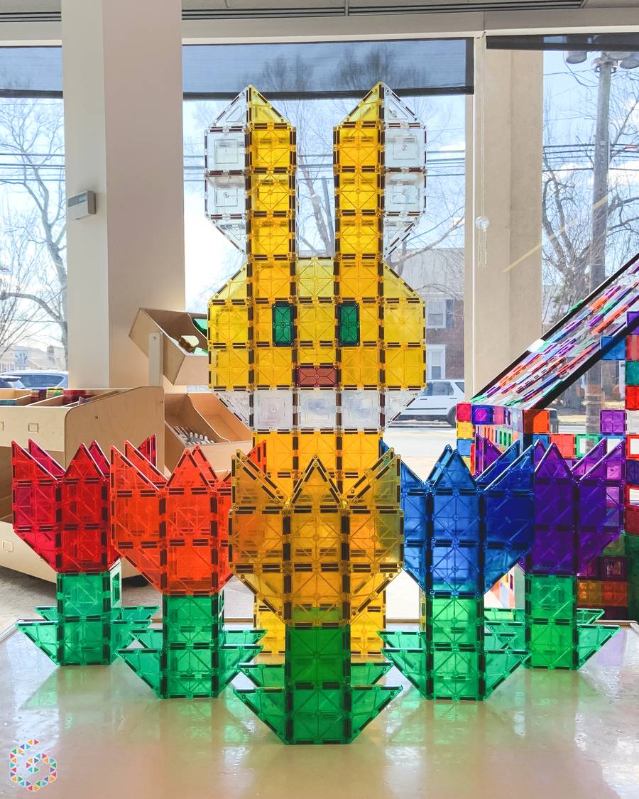 Giant magnetic-tile bunny and colorful tulips built on the floor by a sunlit storefront window