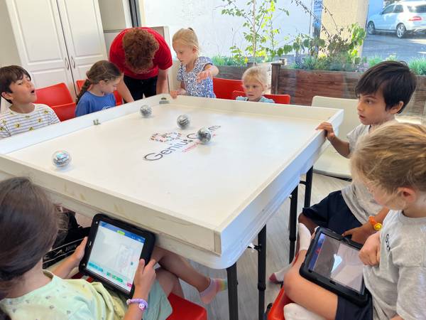 Kids around a white arena table driving Sphero robot balls with iPads at Genius Gems