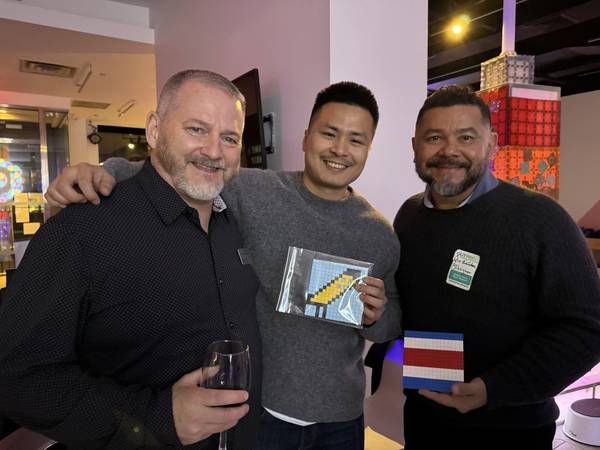 Three adults holding pixel mosaic artworks at an evening event