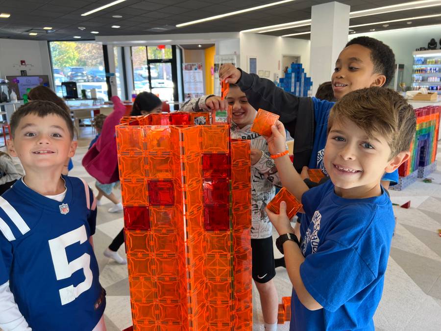 Smiling boy adds an orange magnetic tile to a tall orange and red tile tower