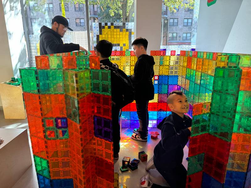 Kids and a grown-up building giant rainbow magnetic tile walls by the storefront windows at Genius Gems NYC