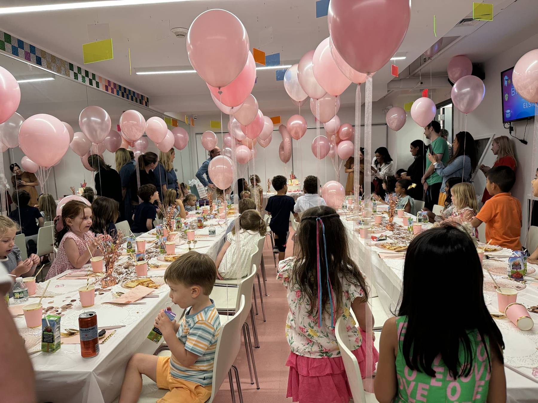 The NYC party room set for a party — long white tables, pink balloons on every table, pizza and juice out