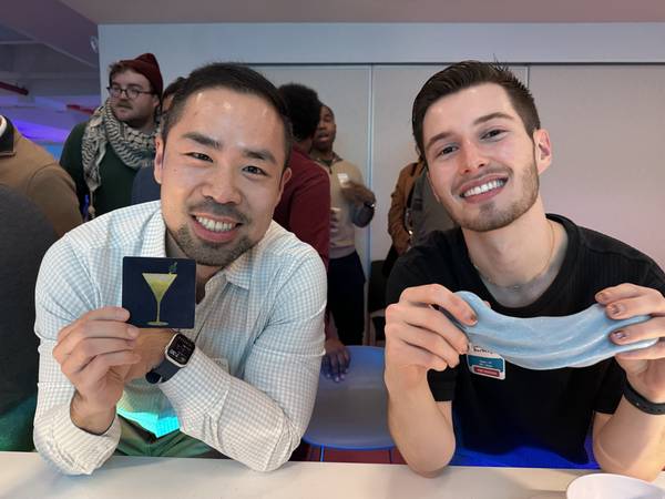 Two adults laughing at a table, one stretching blue glitter slime