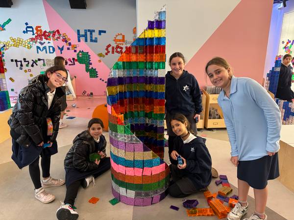 Five girls in school uniforms pose around a tall rainbow magnetic-tile tower