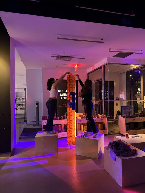 Two adults on wooden platforms building a towering magnetic tile column