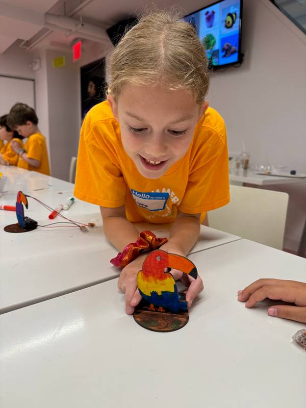 Smiling girl holding a wooden toucan she painted at the Design Bar