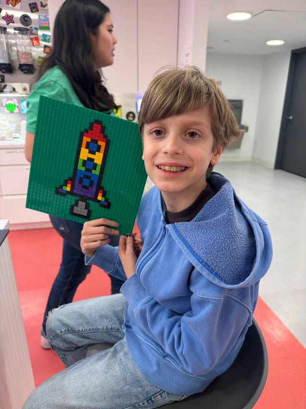 Smiling boy beside a baseplate covered in colorful pixel art mosaic