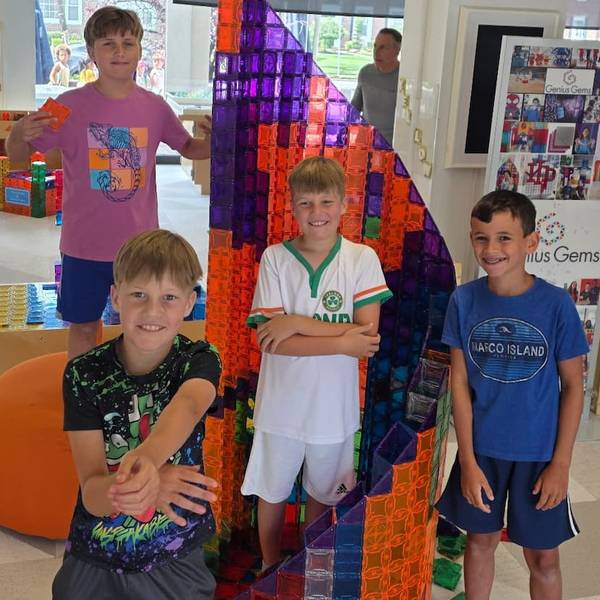 Four smiling kids beside a giant purple and orange magnetic-tile tower