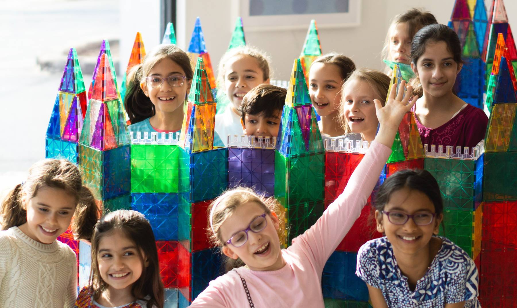 Ten kids beam beside the giant magnetic-tile castle they built together