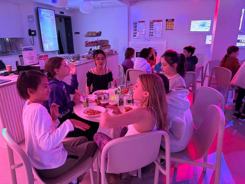 Kids sharing pizza around a table under pink and purple lights