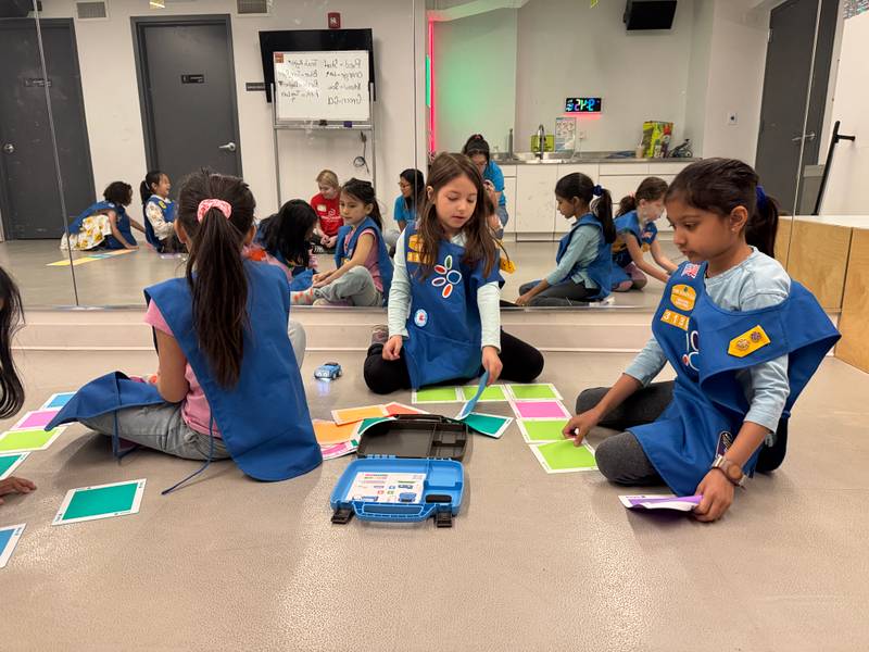 Daisies in blue vests arranging coding cards on the floor beside a robot