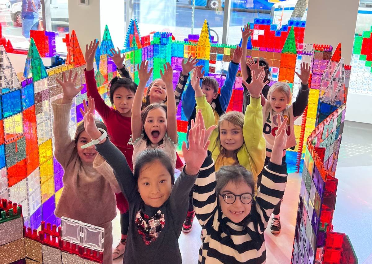 Kids cheering in front of the rainbow tile castle they built together at Genius Gems Millburn