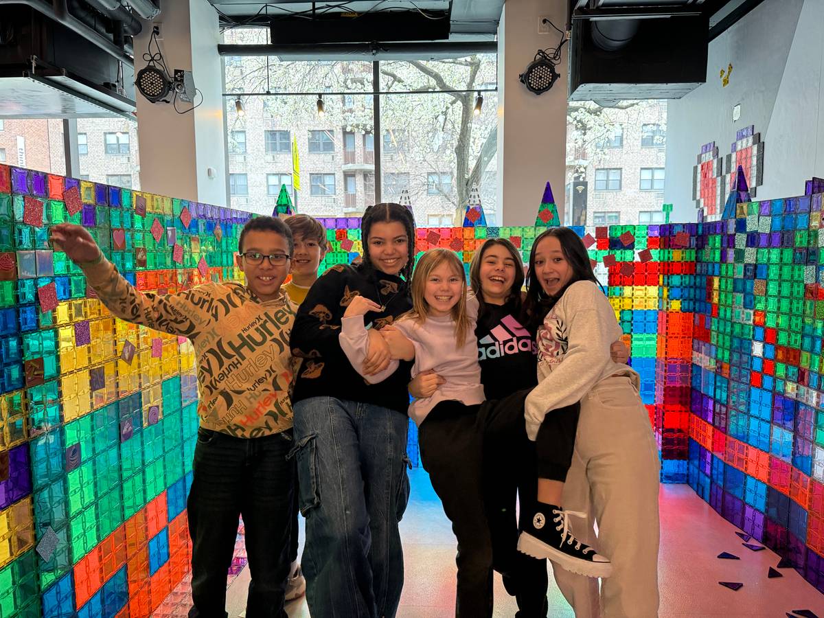Six laughing kids posing together inside a giant rainbow magnetic-tile wall