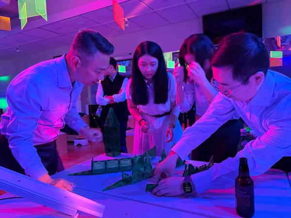 Adults in dress shirts building magnetic tile structures under pink and purple lights