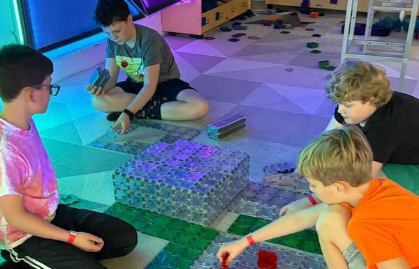 Four kids sitting on the floor building a large flat magnetic-tile structure