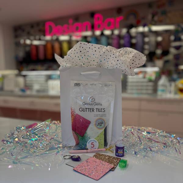 Genius Gems Glitter Tiles gift bag with pink and gold glitter tiles under pink Design Bar neon sign