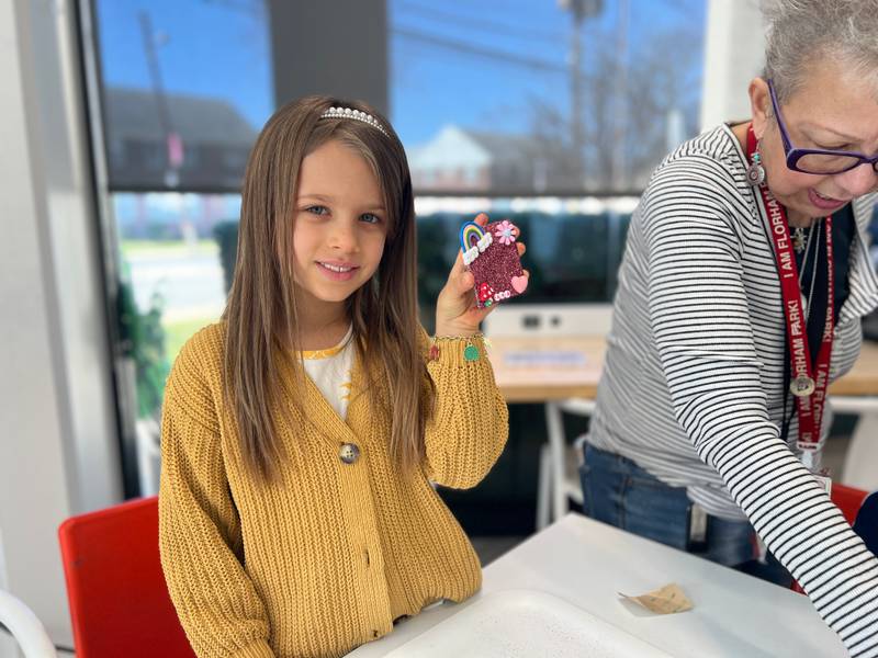A girl holding up a pink glittery Design Bar craft at Genius Gems Millburn