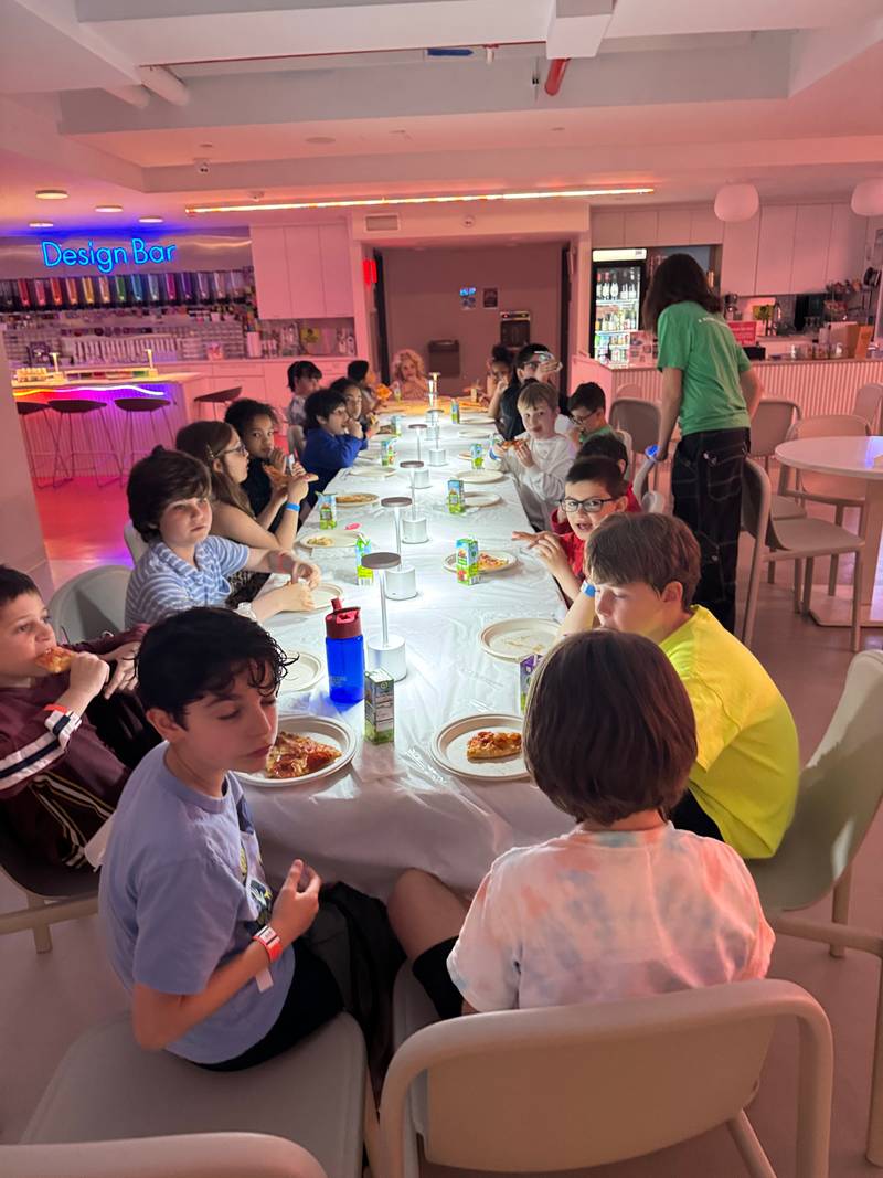 Kids eating pizza dinner at a long table beside the Design Bar at Genius Gems NYC