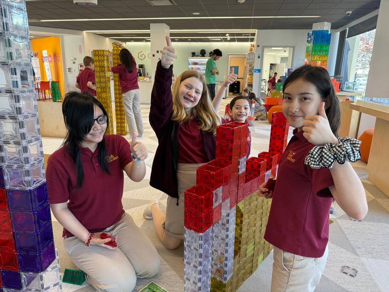 Three girls giving a thumbs up next to red and clear magnetic tile towers at Genius Gems Millburn