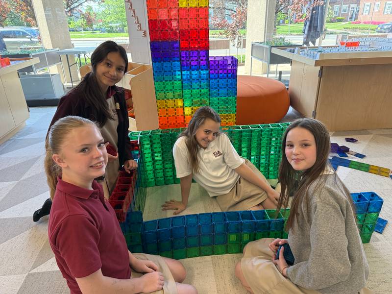 Four girls sitting inside a colourful magnetic tile structure with a rainbow tower behind them at Genius Gems Millburn